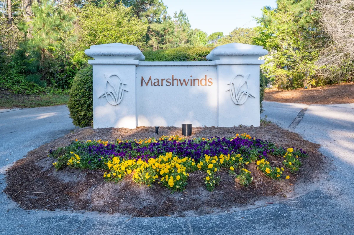 A welcoming community entrance sign surrounded by meticulously maintained flower beds and lush landscaping. The pathway invites residents and visitors to stroll, emphasizing a sense of arrival and belonging within the upscale resort-like community.