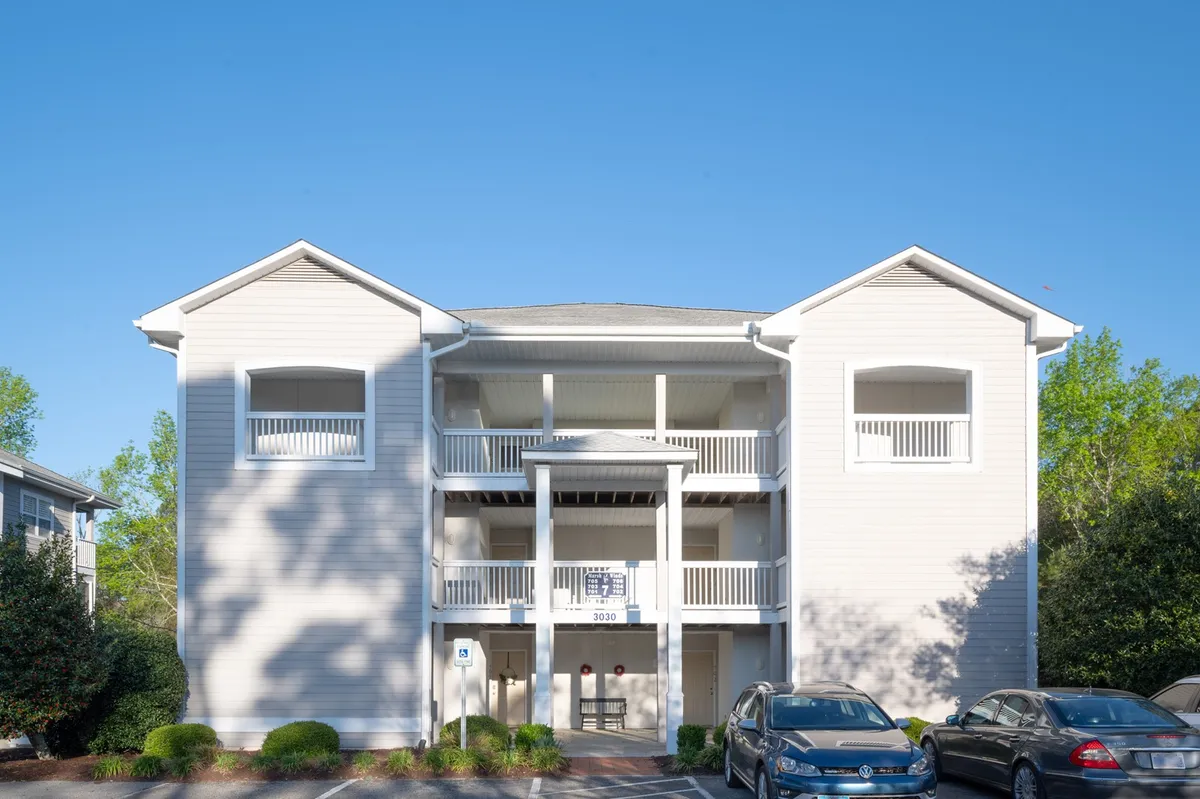 A friendly exterior shot of a two-story building with an entrance sign, parked cars, and manicured bushes. The setup implies easy access to local venues and a communal, open atmosphere ideal for group outings and events.