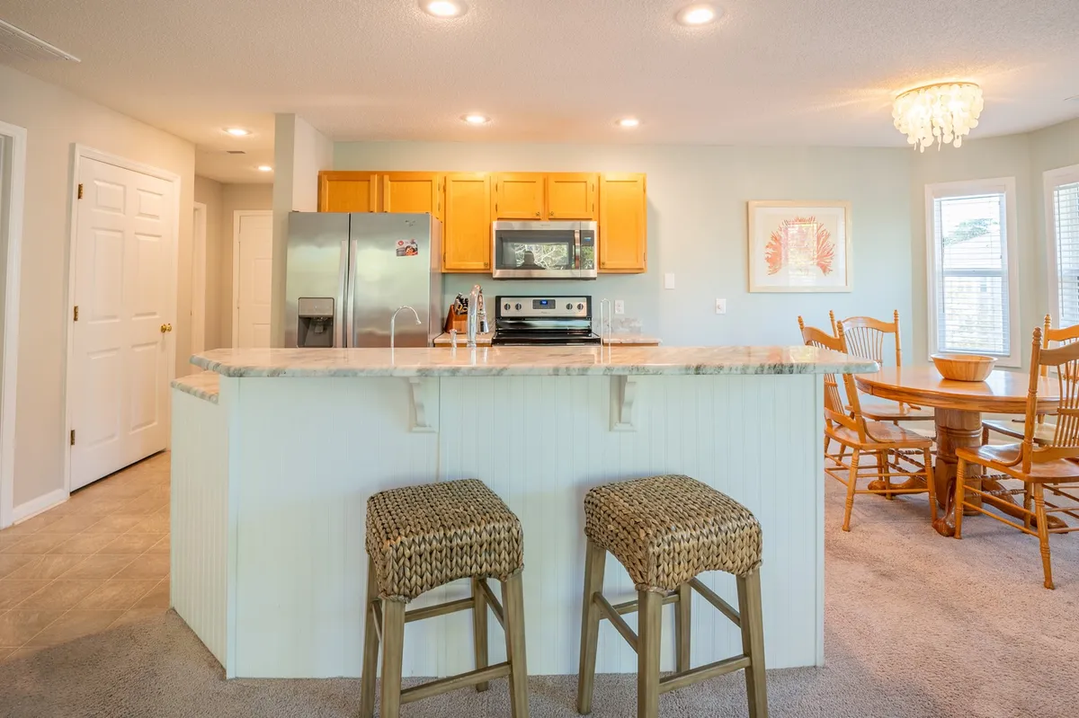 The kitchen and dining area are shown in one integrated, open-concept space. Stainless steel appliances, a generous kitchen island with seating, and a cozy dining table set the stage for both quick breakfasts and celebratory dinners. The layout invites conversation and shared meals under warm lighting.