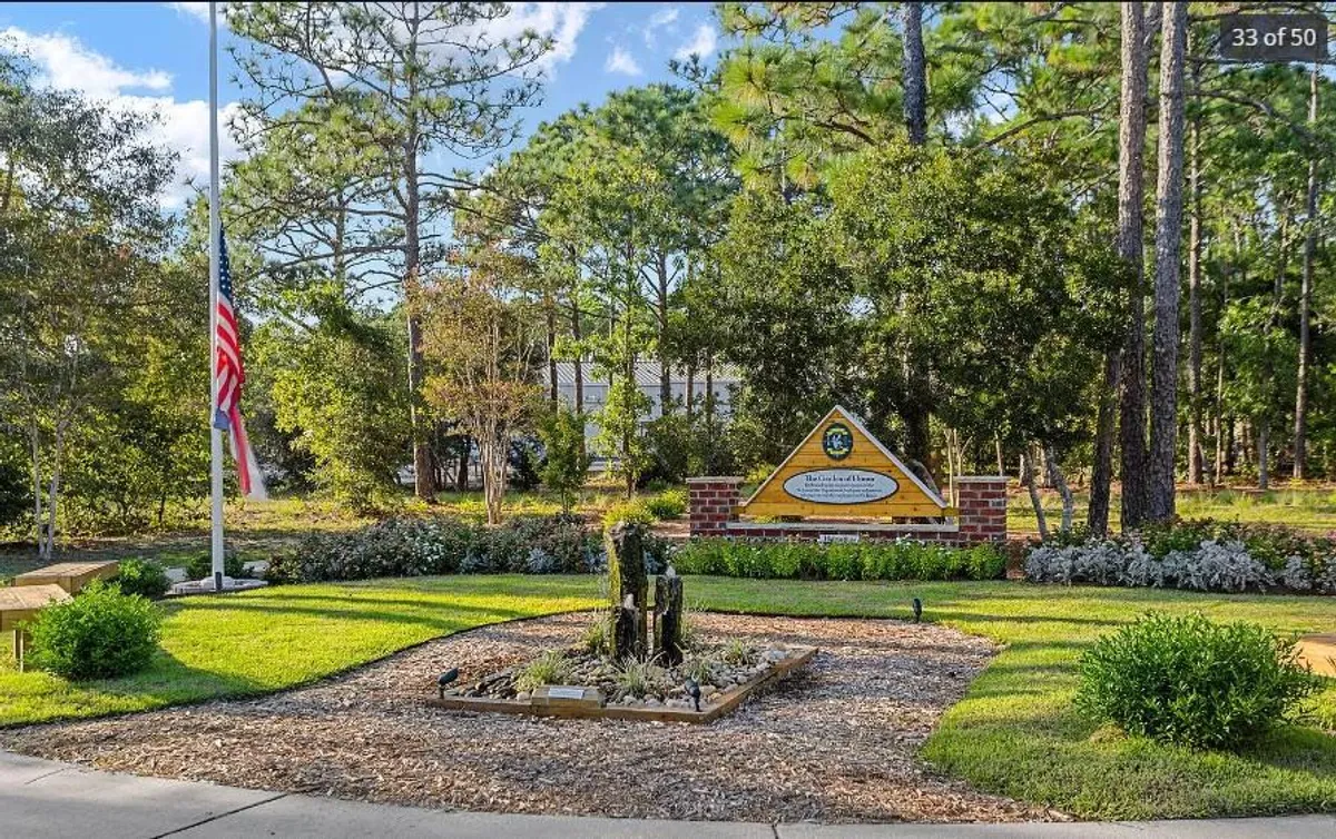This inviting exterior scene features an American flag waving by a welcome sign and landscaped garden, with a pathway suggesting community events or gatherings. The welcoming ambiance and festive details evoke a sense of neighborhood spirit and celebration.