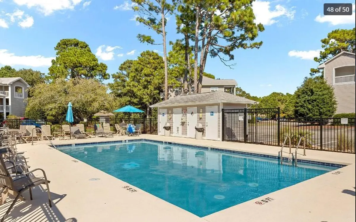This image presents a sparkling outdoor swimming pool surrounded by poolside lounge chairs, umbrellas, and neatly landscaped greenery. The pool area appears inviting and perfect for both relaxation and play, with ample space for families or small groups to unwind under the sun.