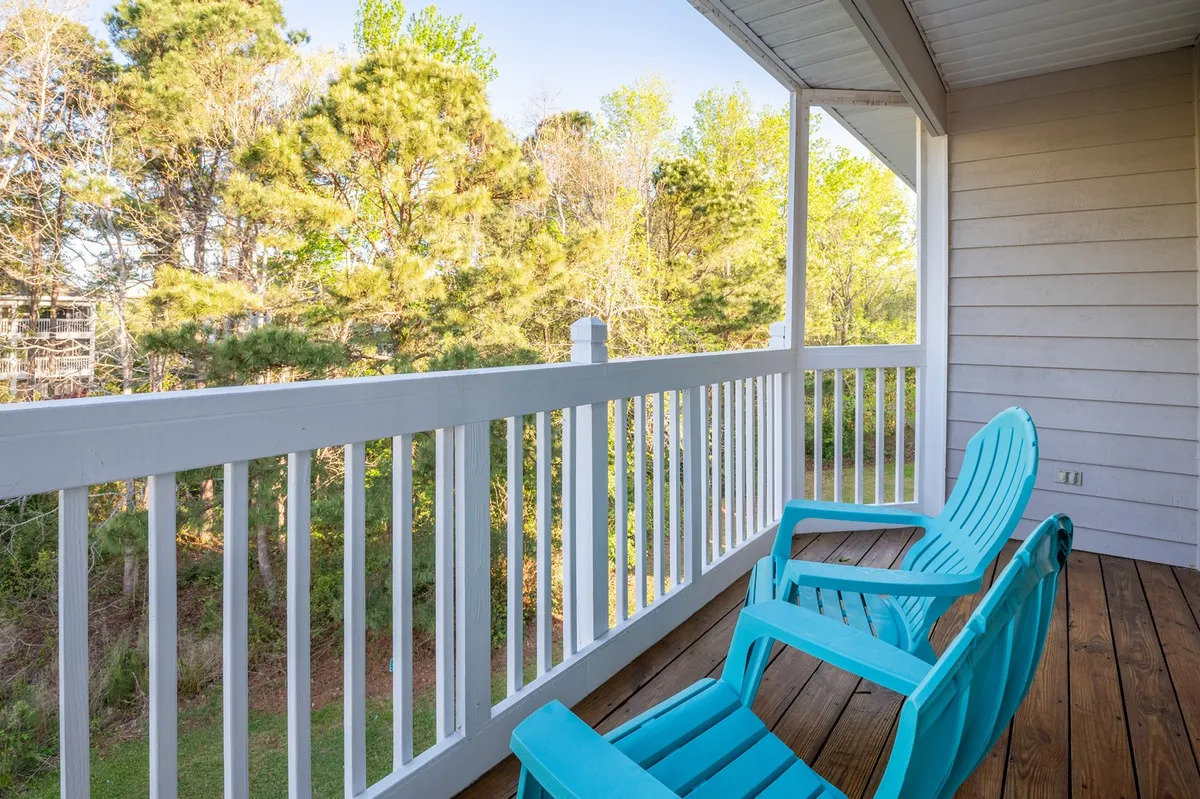 A serene screened-in balcony features bright turquoise chairs and a white railing overlooking lush green trees. The tranquil space invites residents to enjoy morning coffee, unwind with a book, or bask in peaceful sunset views over the waterway.
