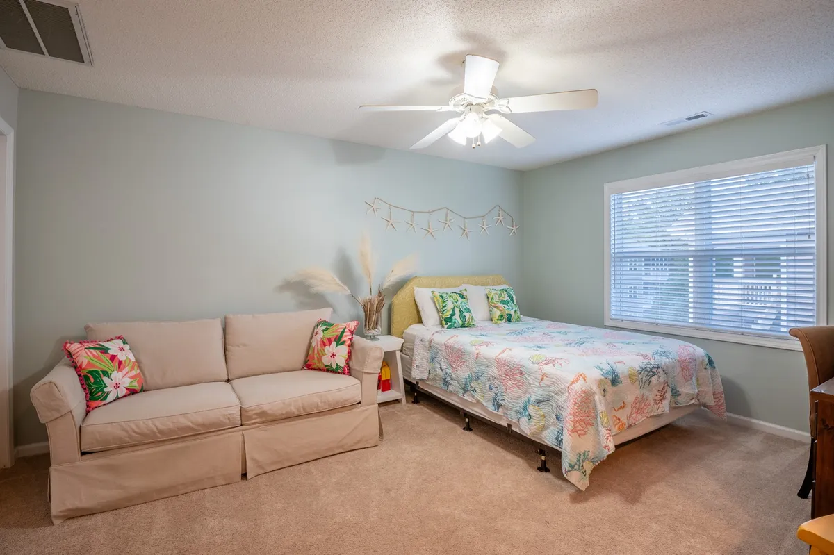 A versatile guest bedroom with a bed featuring colorful bedding and a cozy sofa with decorative pillows situated nearby. The window with blinds provides natural illumination, creating a comfortable and functional retreat within the home.
