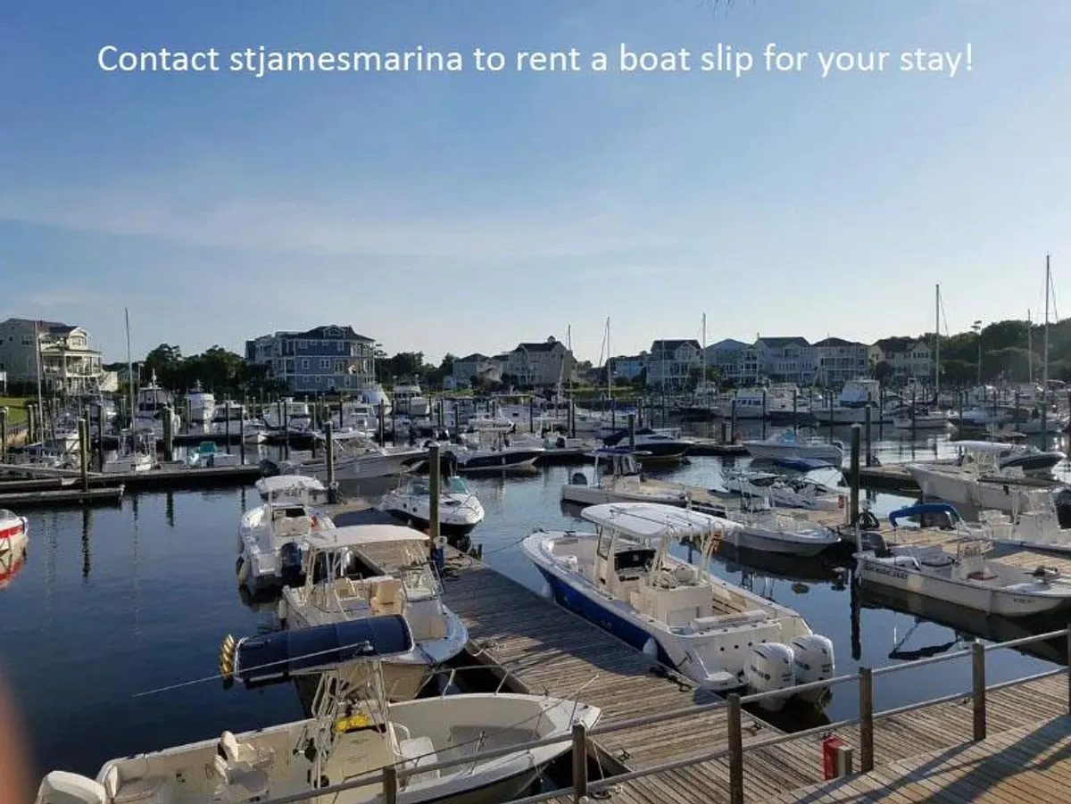 A vibrant marina scene featuring an array of boats docked along a wooden pier, with waterfront buildings creating a picturesque coastal backdrop. The area is bathed in natural light, inviting leisurely strolls, relaxation by the water, or the start of a boating adventure.